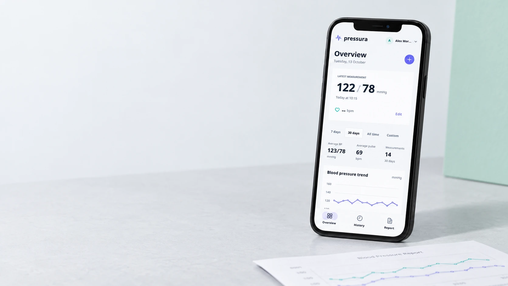 Pressura blood pressure journal on a smartphone beside a printed report, showing sample readings